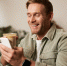 Portrait of smiling charismatic young man, sitting in coffee shop, drinking cappuccino, looking at his mobile phone, reading a message. - Газета Магаданская правда