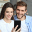 Young couple watching online content in a smart phone sitting on a sofa at home in the living room - Газета Магаданская правда