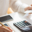 Closeup of person holding bills and calculating them. Notebook, calculator and smartphone lying on desk. Payment concept. Cropped view. - Газета Магаданская правда